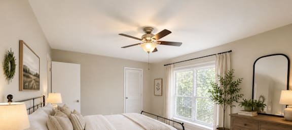 A bedroom with a large bed, a ceiling fan, and a window with a view of trees.