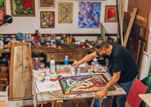 a man working on a painting in a studio with paintings on the wall