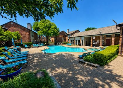 A pool surrounded by lounge chairs and greenery.