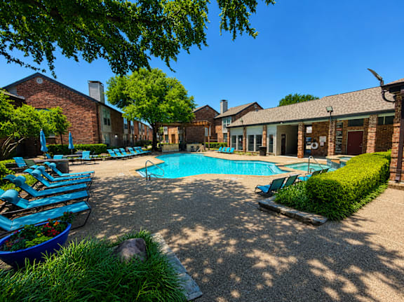 A pool surrounded by lounge chairs and greenery.