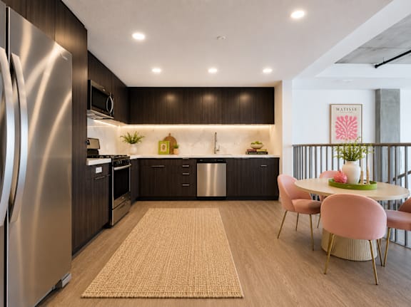 A modern kitchen with a refrigerator on the left and a dining table with chairs in the center at Fusion Hollywood.