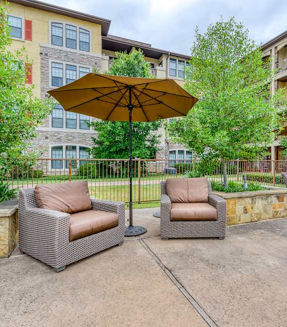 A patio with two chairs and an umbrella in front of a building.