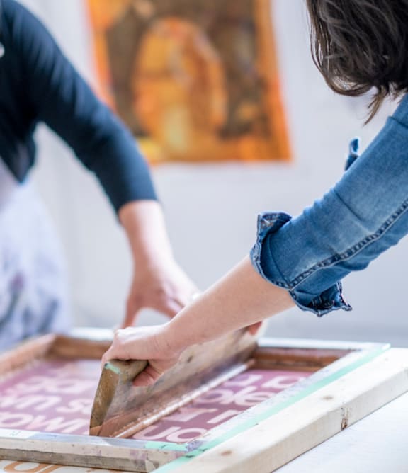 two women working on a large stenciled piece of art