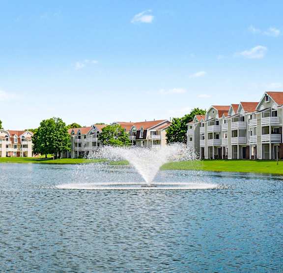 A pond with a fountain surrounded by apartment buildings at Indian Lakes Apartments, Mishawaka, IN, 46545