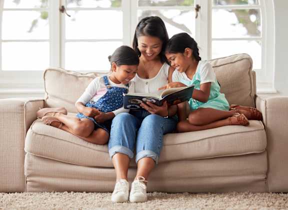 A woman and two children are sitting on a couch reading a book together.