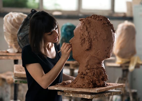 a woman sculpts a clay sculpture in a studio