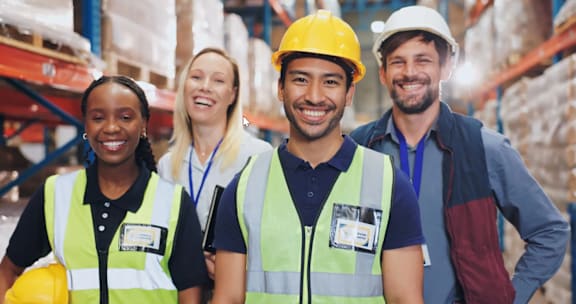 Four people wearing safety vests and hard hats in a warehouse.