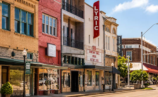 A street view of a city with a red building on the left and a white building with a red sign that says "LYRIC" on the right.