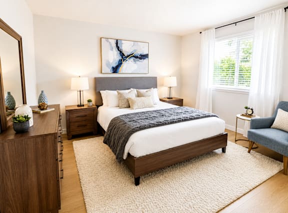 A bedroom with a large bed, a nightstand, a chair, and a painting on the wall.