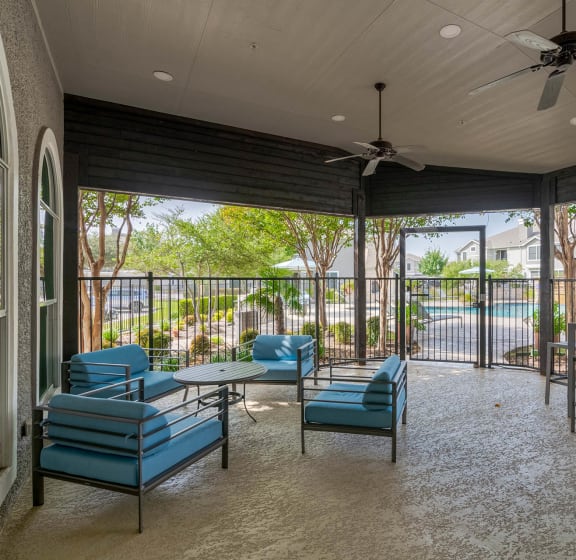 a covered patio with blue chairs and a ceiling fan