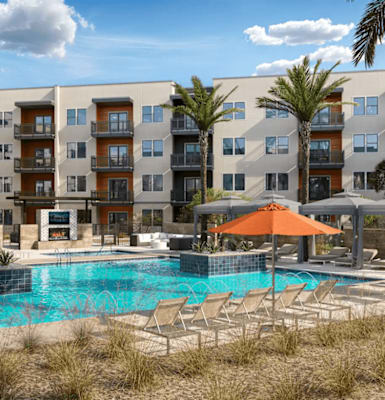 A pool surrounded by chairs and umbrellas in front of apartment buildings.