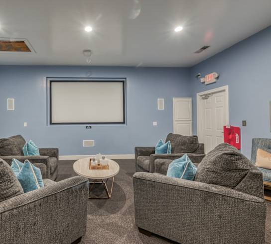 A living room with grey couches and a white screen.