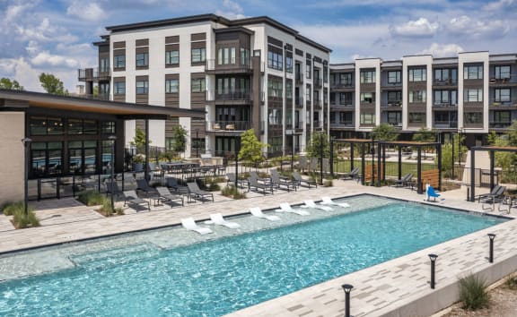 a swimming pool with lounge chairs in front of an apartment building