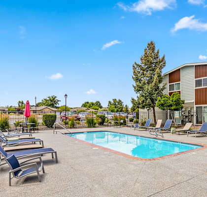 A pool surrounded by lounge chairs and trees at Wildflower Apartments in Kennewick, WA.