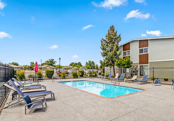 A pool surrounded by lounge chairs and trees at Wildflower Apartments in Kennewick, WA.