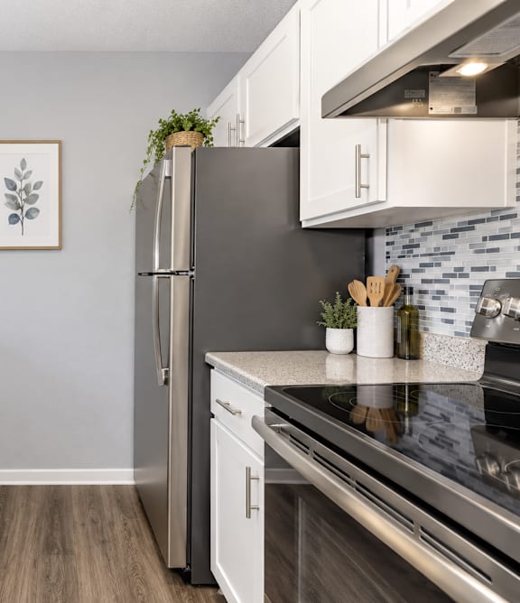 A modern kitchen with a stainless steel refrigerator, white cabinets, and a wooden floor.