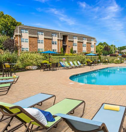 A pool surrounded by chairs and umbrellas with a building in the background.
