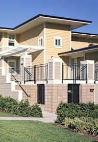 A row of townhouses with balconies and a green lawn in front.