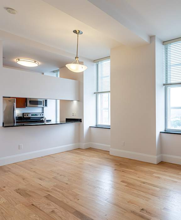 A large empty room with wooden floors and a window with blinds.