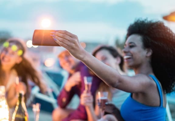 a woman taking a photo of her friends at a beach party with her cell phone