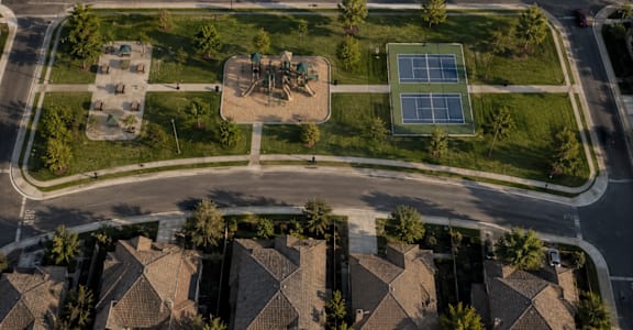 A tennis court is located in the middle of a grassy area in a residential neighborhood.