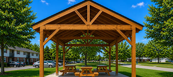 A wooden pavilion with picnic tables is situated in a grassy area.