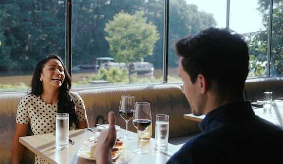 A man and a woman are sitting at a table with drinks and food in front of them. and a view of the Sam Patch tour boat going by on the canal outside the window