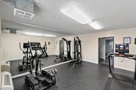 A gym with treadmilers, elliptical machines, and a weight rack.