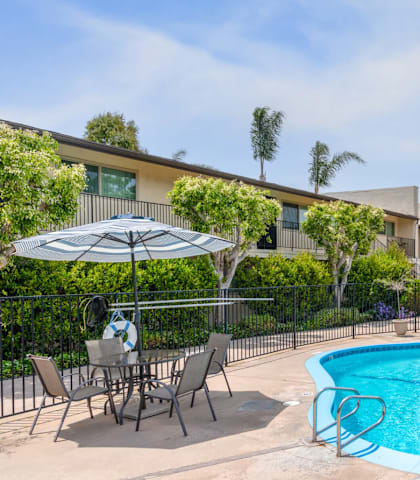 A swimming pool surrounded by chairs and umbrellas in front of a building.