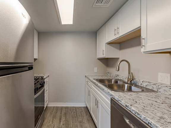 A kitchen with a stainless steel refrigerator, a stove, and a marble countertop.