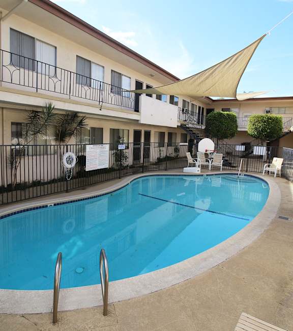 A pool with a hot tub and lounge chairs in front of a building.