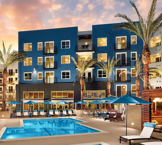 A large swimming pool in front of a multi-story building with palm trees.
