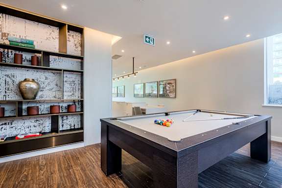 A pool table in a room with a shelf of vases and pictures on the wall.