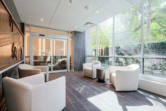A modern waiting room with white chairs and a view of trees outside.