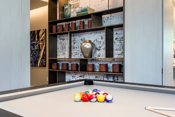 A pool table with balls and a cue stick in front of a wall with shelves and decorations.