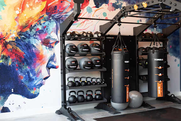 A gym with a punching bag, kettlebells, and a wall mural.