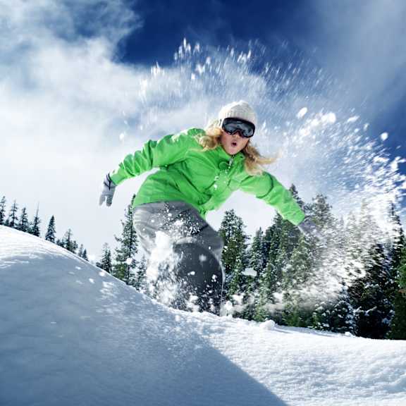A person in a green jacket and white hat is snowboarding down a snowy hill.