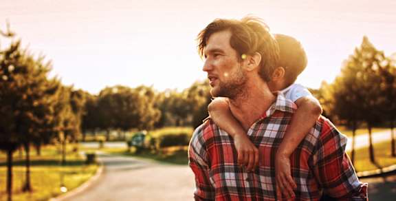 A man in a plaid shirt is carrying a child on his back.