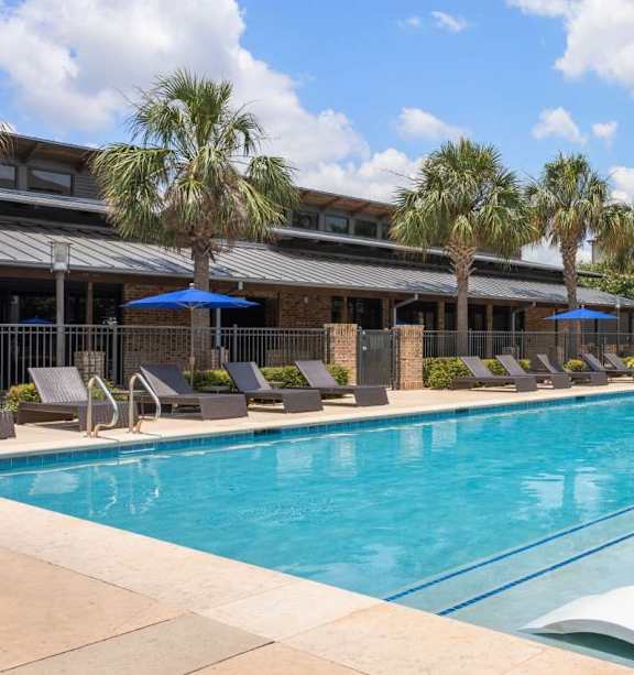 A large swimming pool with lounge chairs and umbrellas in front of a building.