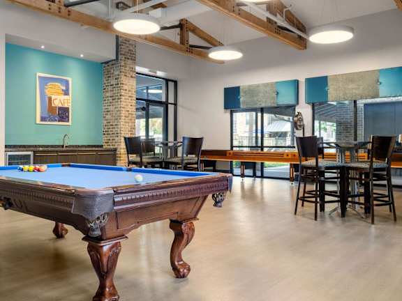 A pool table is in the middle of a room with a brick pillar and a blue wall.