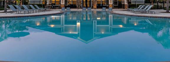 A large swimming pool in front of a house with lounge chairs and umbrellas.