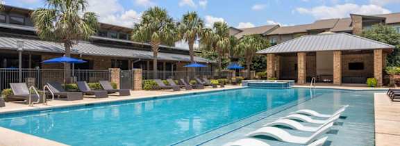 A large swimming pool with lounge chairs and umbrellas in front of a building.