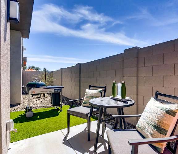 A patio with a table, chairs, and a bottle of wine.