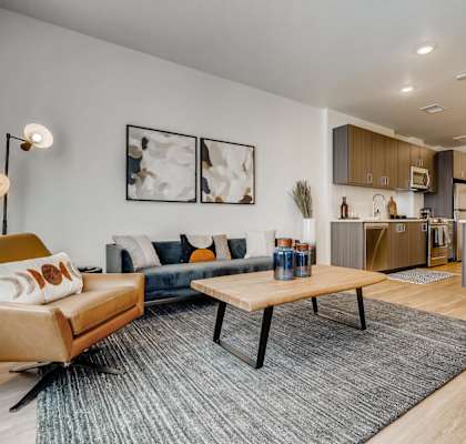 A modern living room with a blue couch, a wooden coffee table, and a kitchen area in the background.