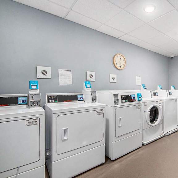 a laundromat with a row of washers and dryers and a clock