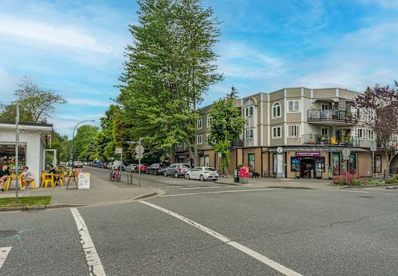 A street view of a residential area with apartment buildings and cars parked on the side of the road.
