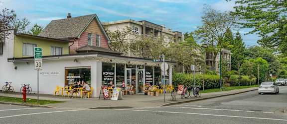A street view with a building on the left and a car on the road.