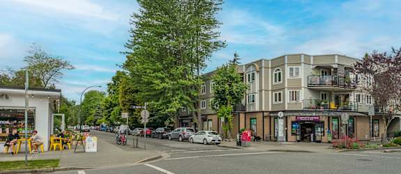 A street view of a residential area with apartment buildings and cars parked on the side of the road.