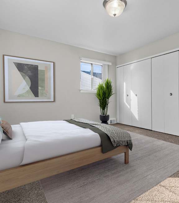 A bedroom with a bed, a plant, and a framed picture on the wall.