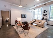 Thumbnail 7 of 22 - A living room with a white couch, a wooden table, and a TV mounted on the wall.